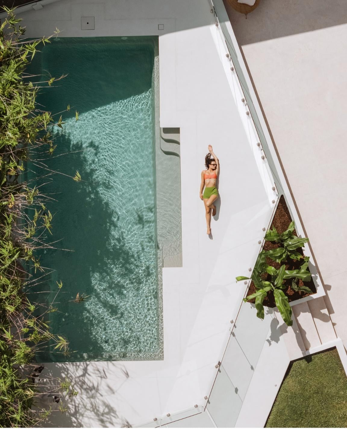 Aerial view of a white microcement pool surround with sun deck and tropical planting